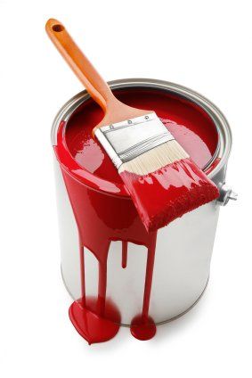 a paint can with a brush in it and red liquid pouring out of the top