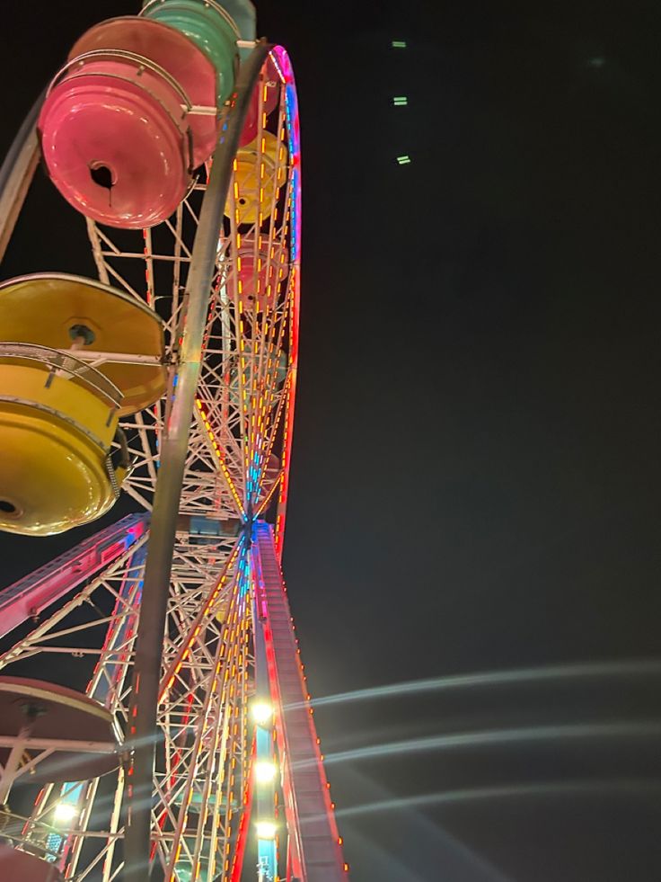 the ferris wheel is lit up at night with colorful lights on it's sides