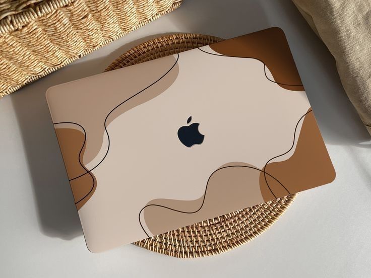 an apple laptop sitting on top of a table next to a wicker basket and pillow