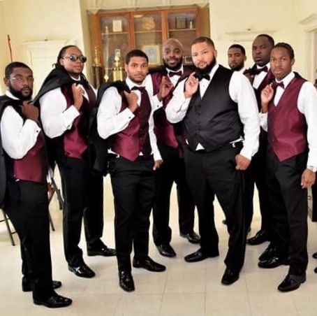 a group of men standing next to each other in front of a door wearing red vests and bow ties