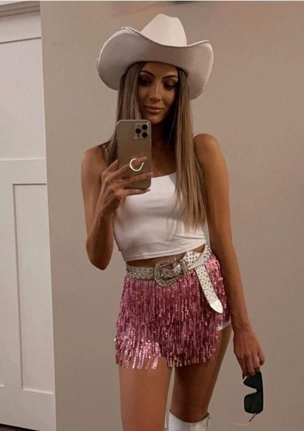 a woman wearing a cowboy hat and fringe skirt taking a selfie in the mirror