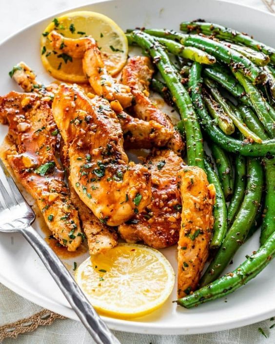 grilled chicken, green beans and lemon on a white plate with a silver fork