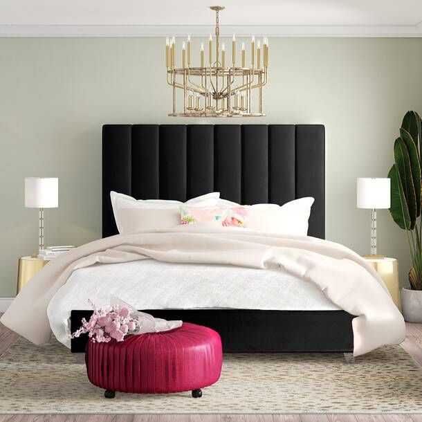 a bedroom with a large bed, chandelier and pink footstool on the floor