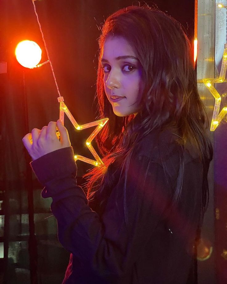 a woman standing in front of a window holding onto a star shaped string with lights on it