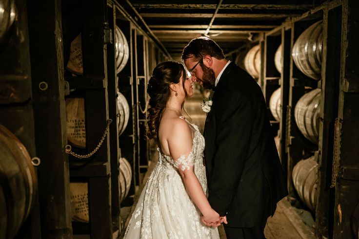 a bride and groom standing next to each other in front of some wine casks