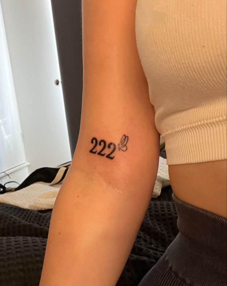 a woman's arm with a small tattoo on it that reads 22 and has a butterfly