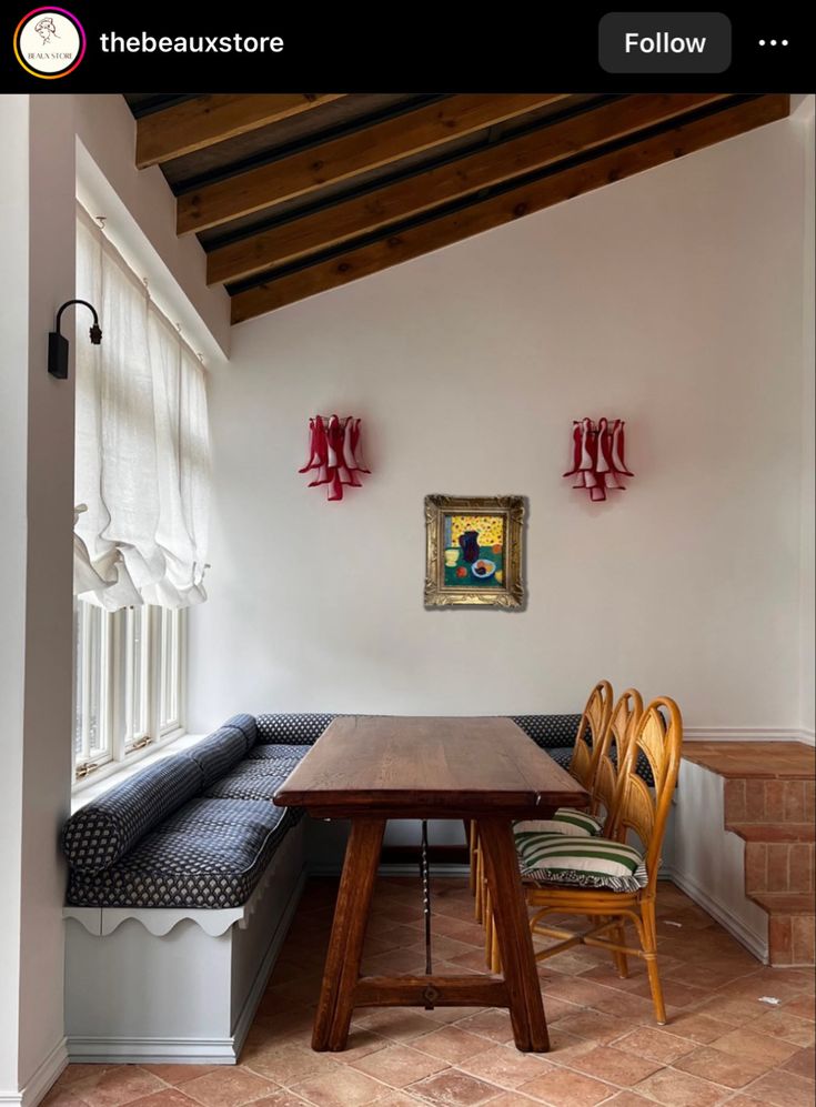 a wooden table sitting under a window next to a bench with two chairs on it