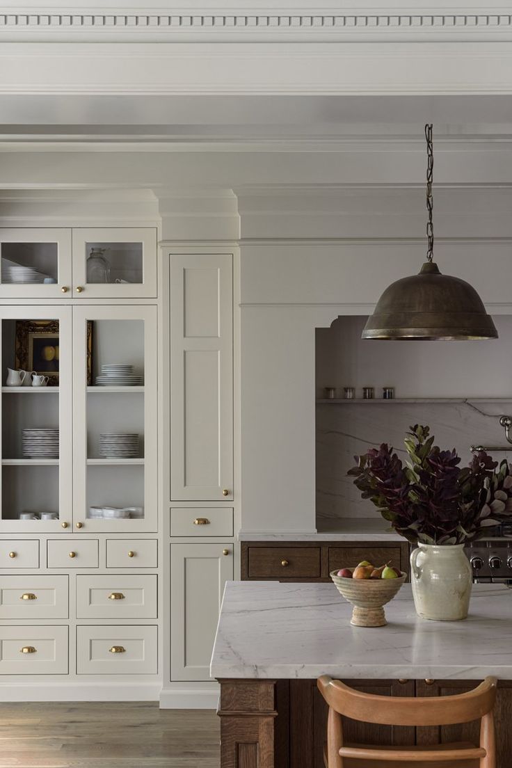 a kitchen with white cabinets and marble counter tops, an island in the middle is surrounded by wooden chairs