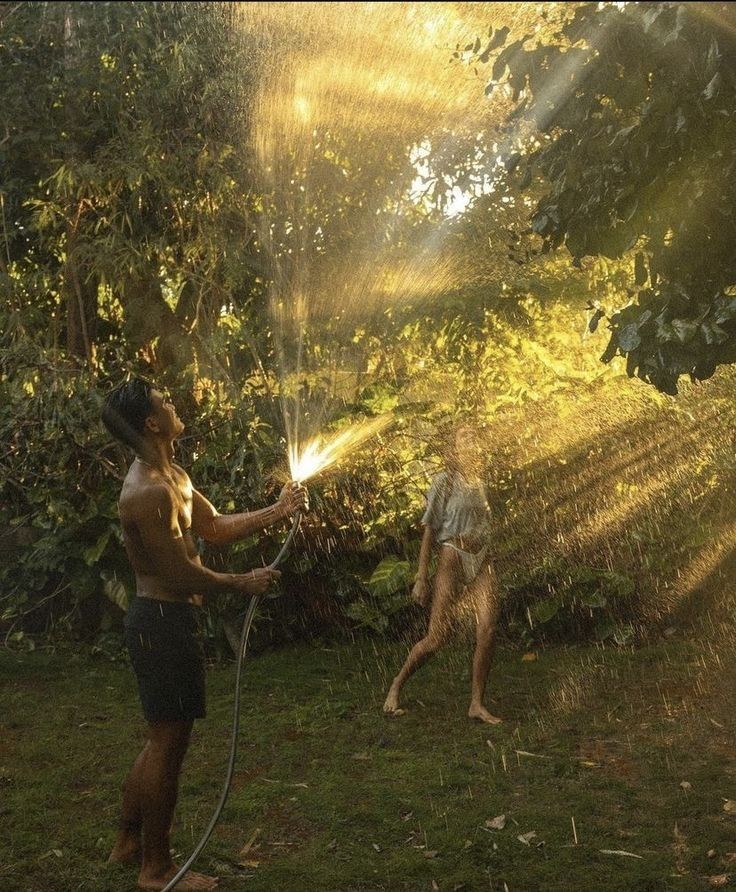 a man is spraying water on his dog in the yard while he plays with it