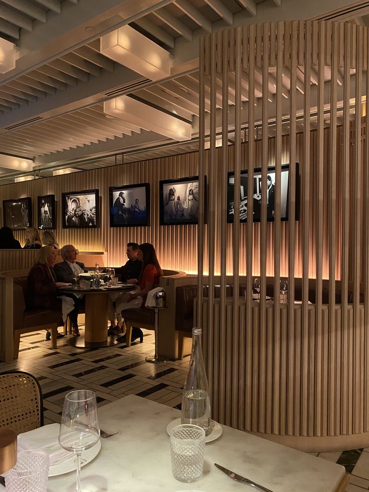 people sitting at tables in a restaurant with wooden slats on the wall behind them