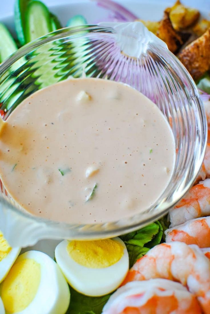 a bowl filled with dressing next to sliced cucumbers and shrimp