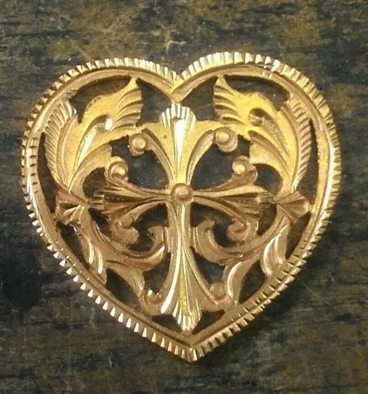 a gold heart shaped brooch sitting on top of a wooden table in front of a wall