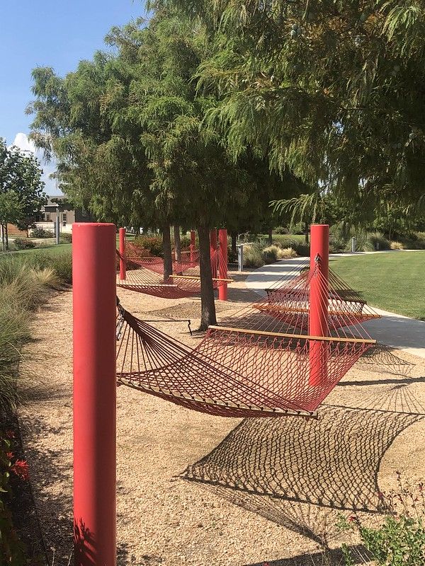 there is a hammock in the park with red poles and trees around it