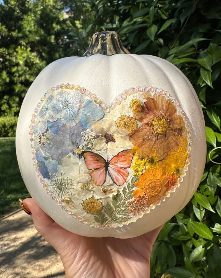 a person holding up a painted pumpkin with flowers and butterflies in the shape of a heart