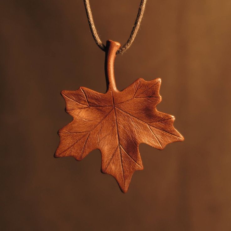 an oak leaf is hanging from a cord on a brown background with a black bead