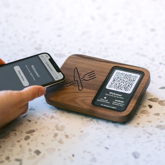 a person holding a cell phone next to a wooden cutting board with qr code on it