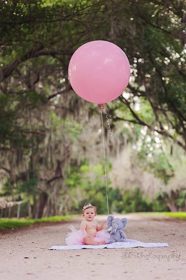 a baby sitting on a blanket with a pink balloon