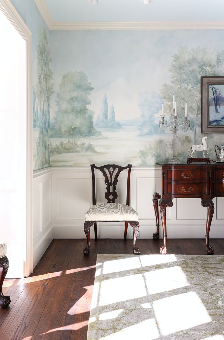 two chairs and a table in front of a wall with a landscape painted on it