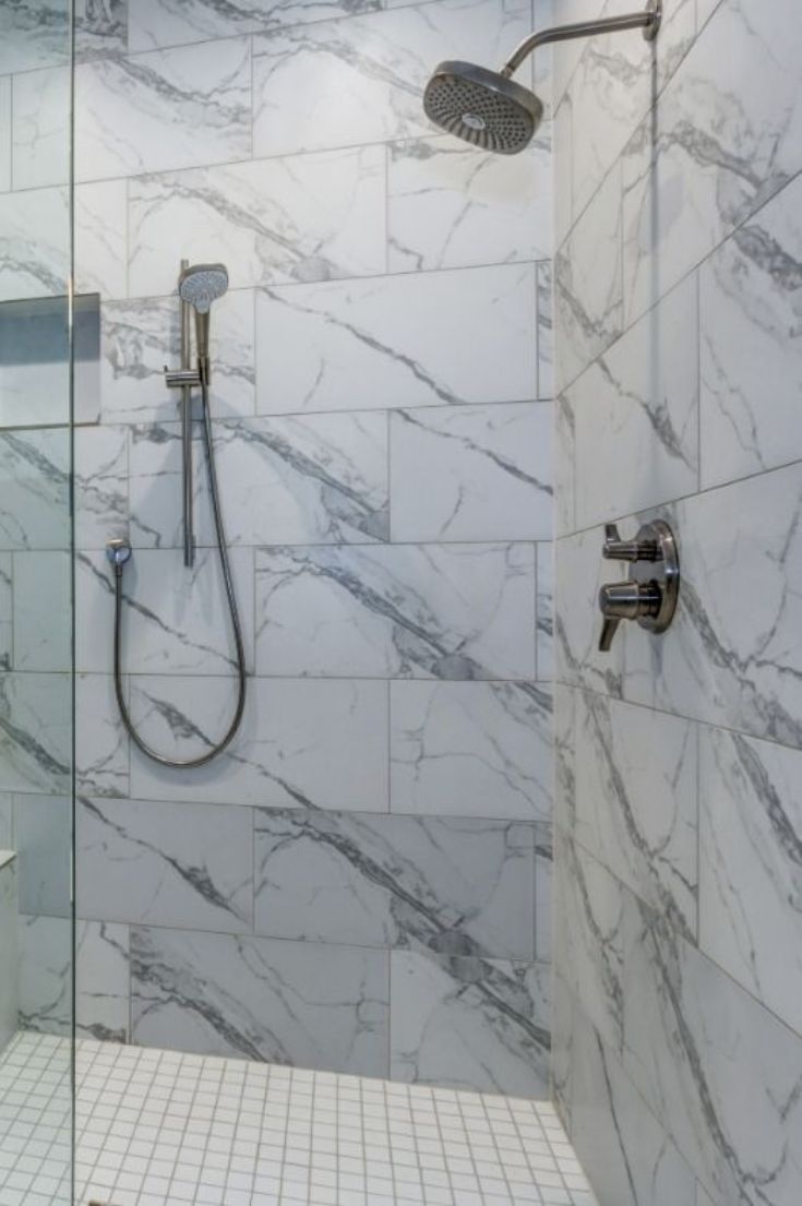 a bathroom with marble walls and flooring, shower head and hand held shower faucet