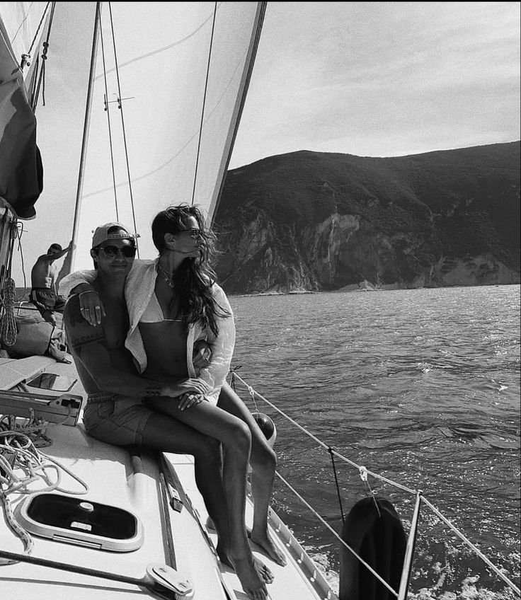 a man and woman sitting on the back of a sailboat