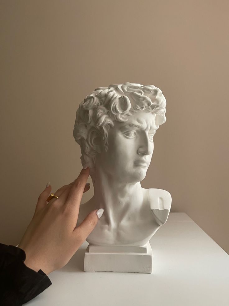 a person touching the face of a white busturine on top of a table