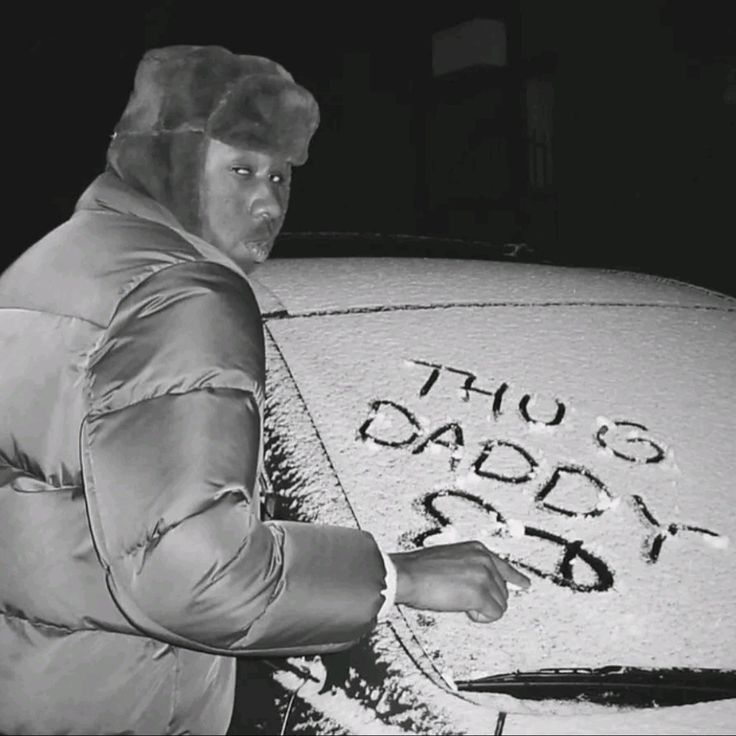 a man standing next to a car covered in snow with writing on the hood and windshield