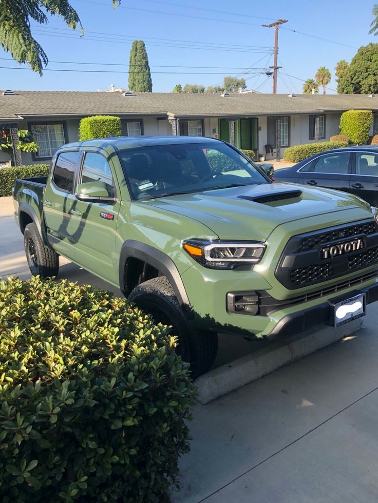 a green toyota pickup truck parked in front of a house with two cars behind it