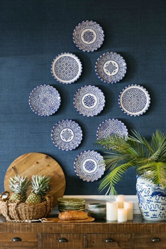 blue and white plates hanging on the wall above a wooden dresser with pineapples