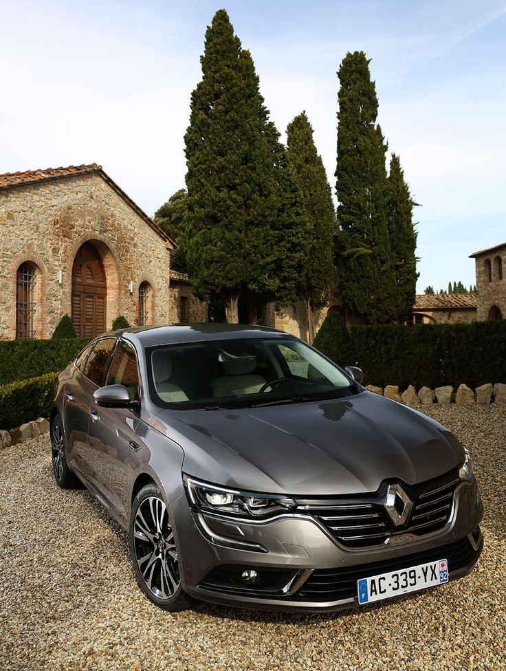 a grey car parked in front of a stone building with trees and bushes around it