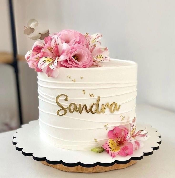 there is a white cake with pink flowers on the top and gold lettering that says sandra