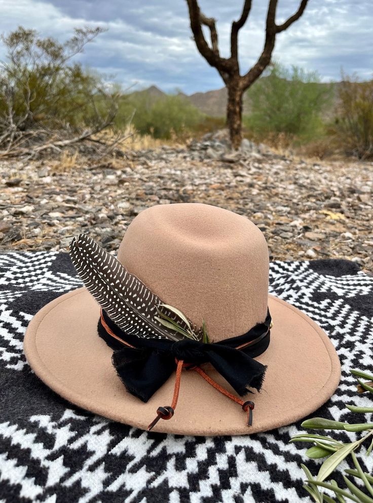 This tan felt hat is complimented with a rugged black band and a rust leather tie. It is accented with brass and carved bone beads and a turkey feather and dried olive leaves.  Wander in the desert. Rustic Adjustable Hats For Fall, Rustic Adjustable Felt Hat For Festival, Rustic Brown Felt Hat For Outdoors, Rustic Brown Felt Hat For Outdoor, Adjustable Brown Hat Bands For Fall, Western Style Felt Hunting Hat For Fall, Rustic Adjustable Hat For Hunting, Rustic Hat Bands For Outdoor Fall, Rustic Hat Bands For Outdoor Fall Season