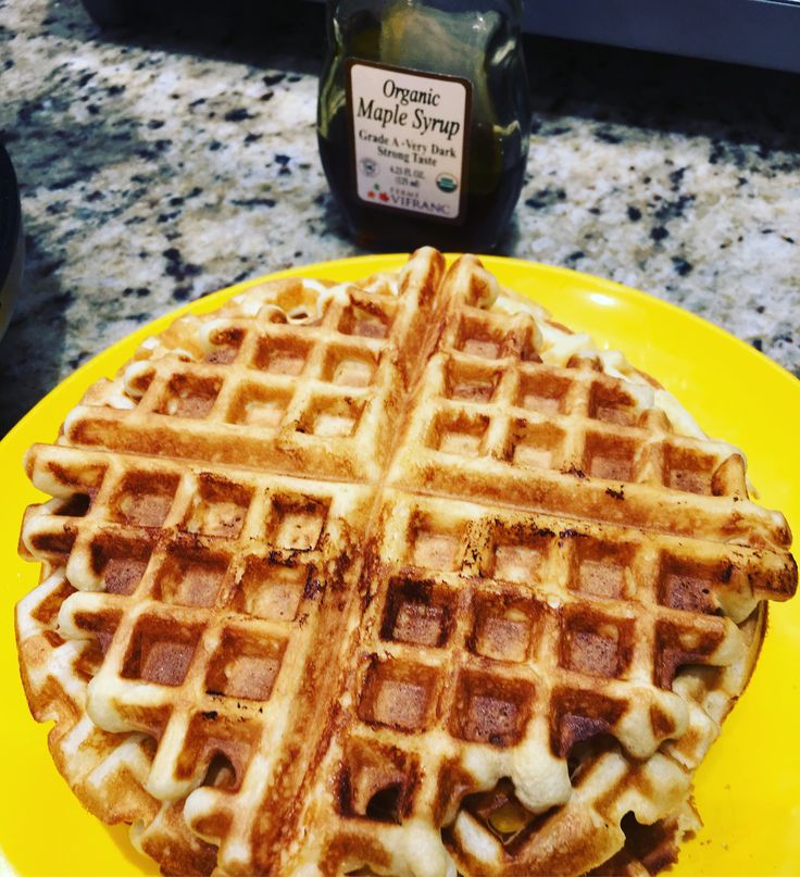 a yellow plate topped with waffles on top of a counter next to a bottle of maple syrup