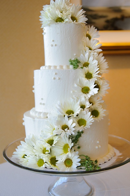 a wedding cake with daisies on the top and bottom tier is sitting on a glass platter