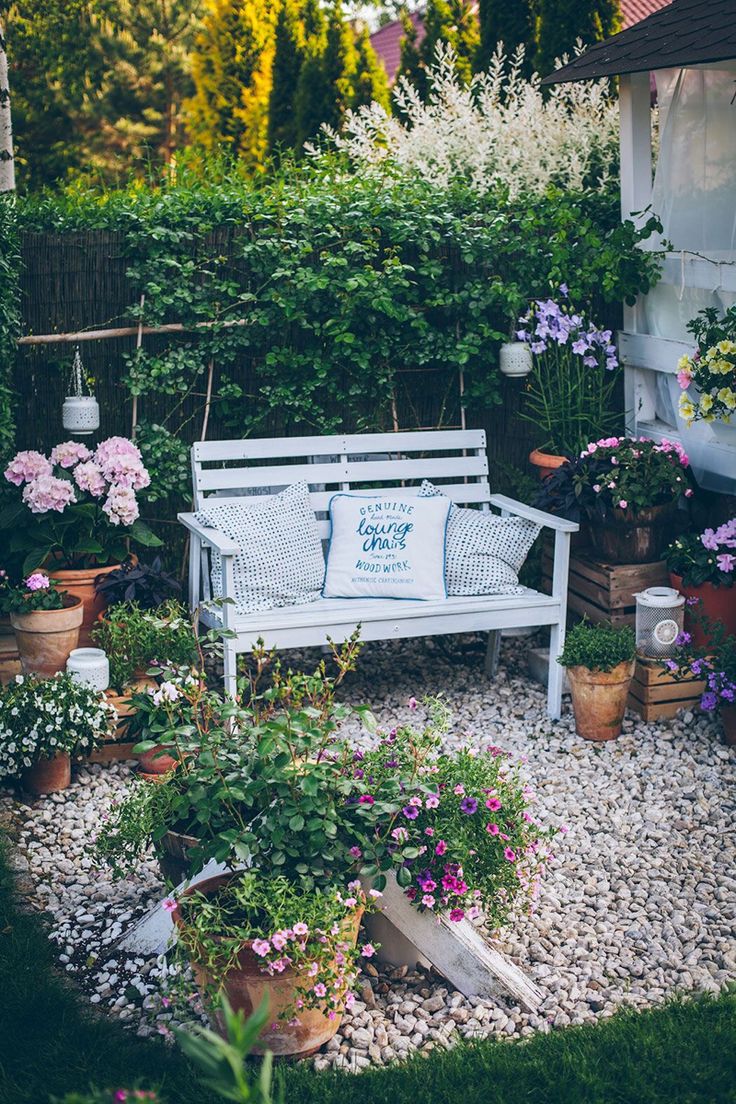 a white bench sitting in the middle of a garden filled with potted plants and flowers