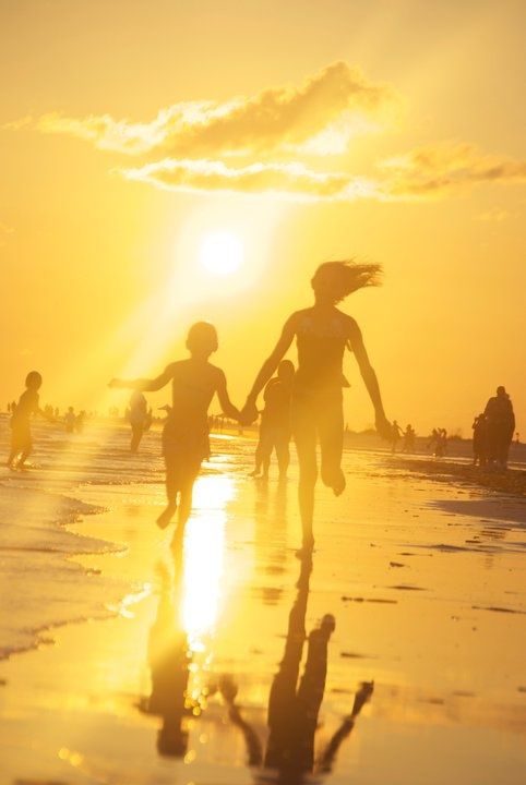 people are running on the beach at sunset