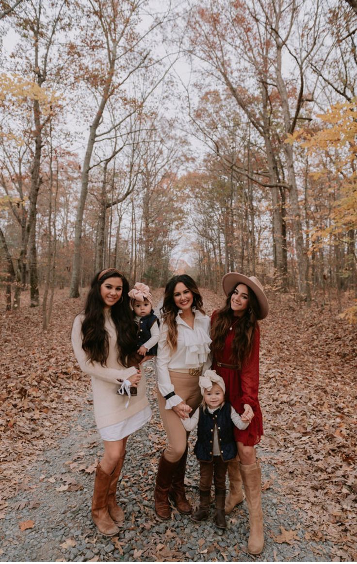 three women and a baby are posing for a photo in the woods with leaves on the ground