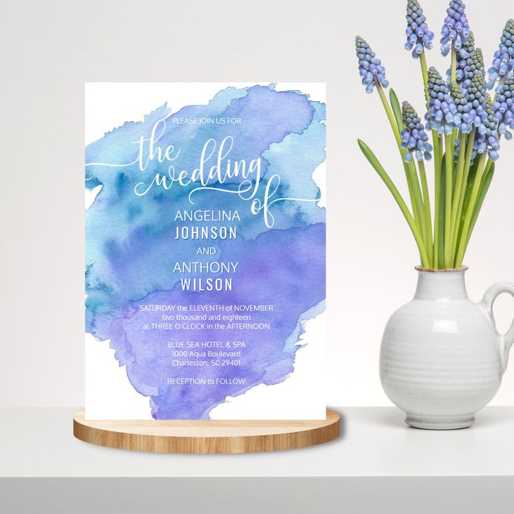 the wedding card is next to a vase with lavenders in it on a table