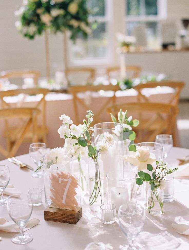 the table is set with white and green flowers in vases, wine glasses, and napkins