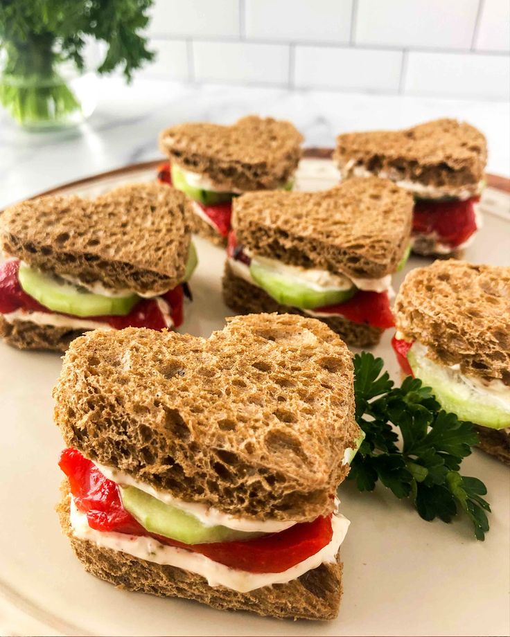 several sandwiches are arranged on a plate with cucumber and tomato slices in the middle