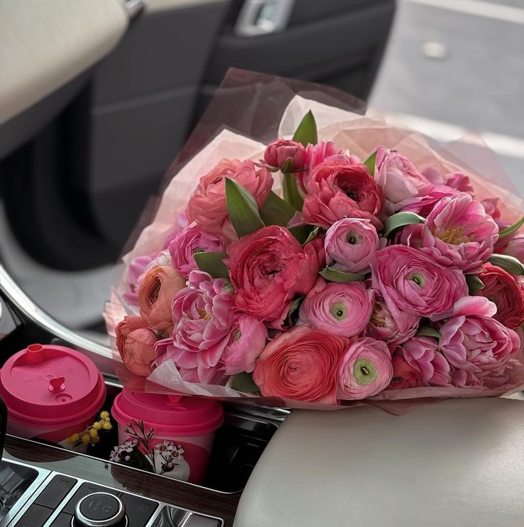 a bouquet of pink flowers sitting on top of a car dashboard next to a cup