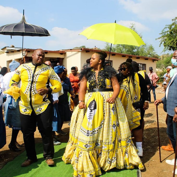 a group of people standing next to each other on a green field with an umbrella