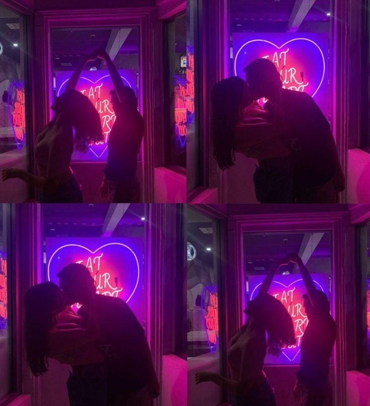 a man and woman kissing in front of a window with neon signs on it at night