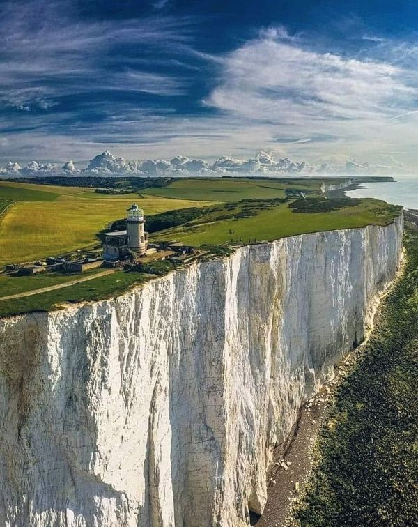 an aerial view of the white cliffs and lighthouses on the cliff face, with blue skies in the background