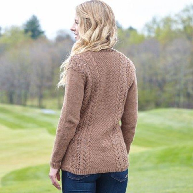 a woman standing on top of a golf course wearing a brown cardigan sweater and jeans