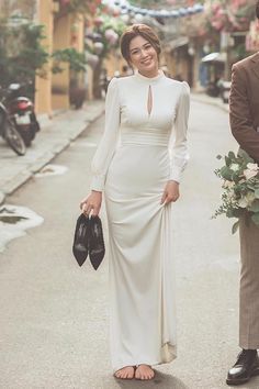 a man standing next to a woman in a white dress and holding a black purse