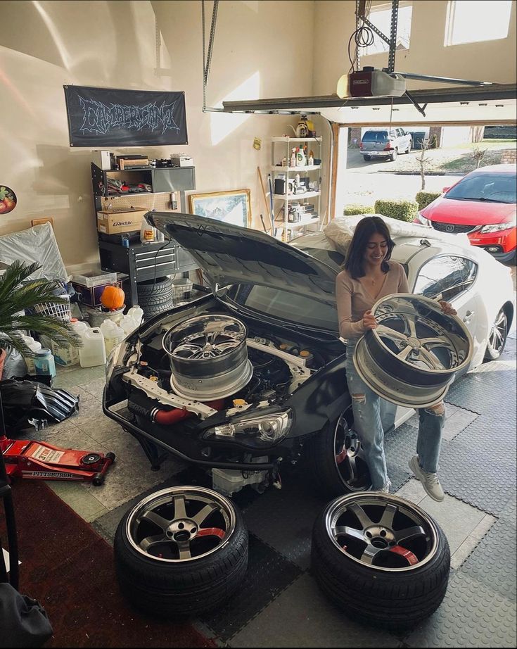 a woman standing next to a car with its hood open and two tires on the ground