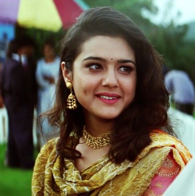 a woman in a yellow sari and gold jewelry smiling at the camera with people behind her