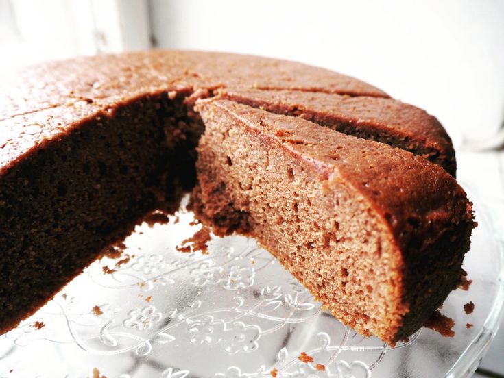 a chocolate cake with one slice missing from it on a glass platter next to a window