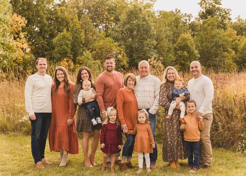 a large family posing for a photo in the grass with trees in the back ground