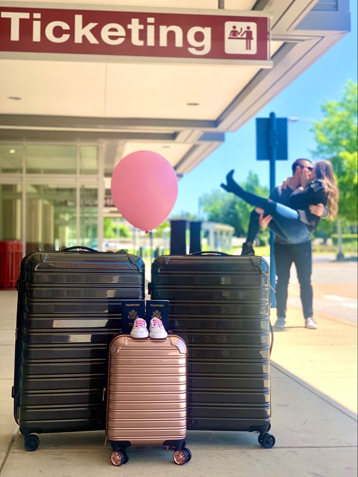 two pieces of luggage sitting on the sidewalk in front of a ticketing station sign